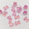A collection of small, pink, translucent plastic beads shaped like teddy bears and bows, featuring an iridescent, holographic finish on a plain white background.