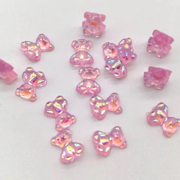 A collection of small, pink, translucent plastic beads shaped like teddy bears and bows, featuring an iridescent, holographic finish on a plain white background.