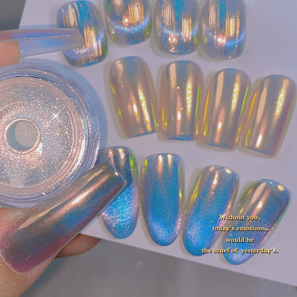 A hand holds a small clear jar of iridescent nail powder next to a sheet of false nails showing the product effect. The nails have a holographic finish shifting between blue, silver, pink, and gold, with Chinese text overlaid on the top left.